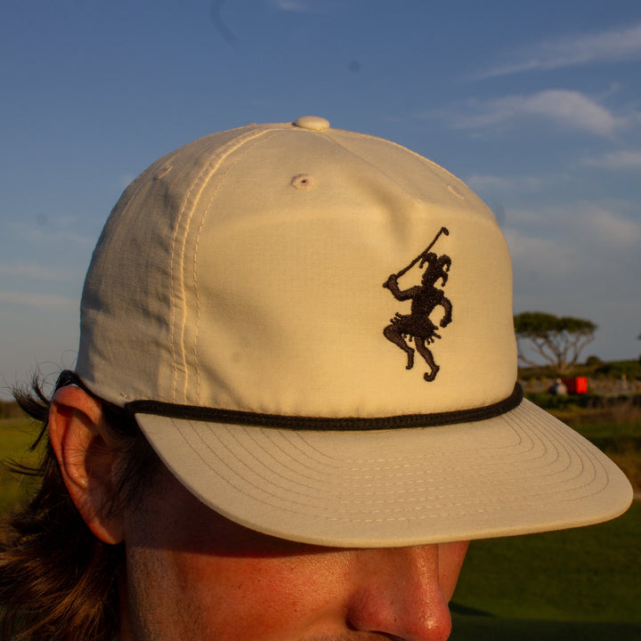 A golfer wearing the white golf hat with two embroidered logos and a black rope.