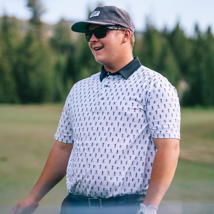 A golfer wearing a white golf polo with a black collar. The polo has a pattern of stick figure golfers.