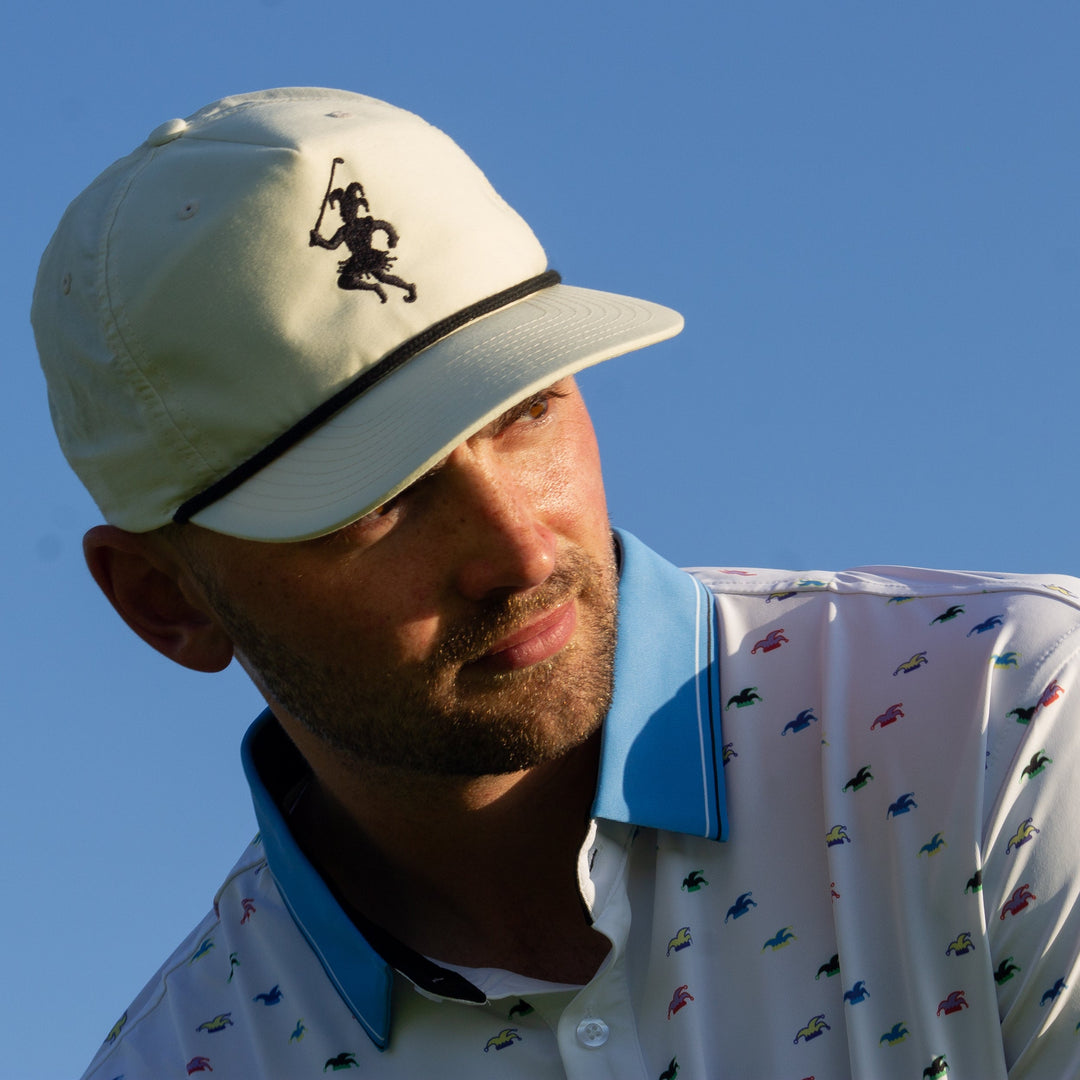 A golfer wearing a white polo with a blue collar and a white performance hat stares down a shot he is about to hit.