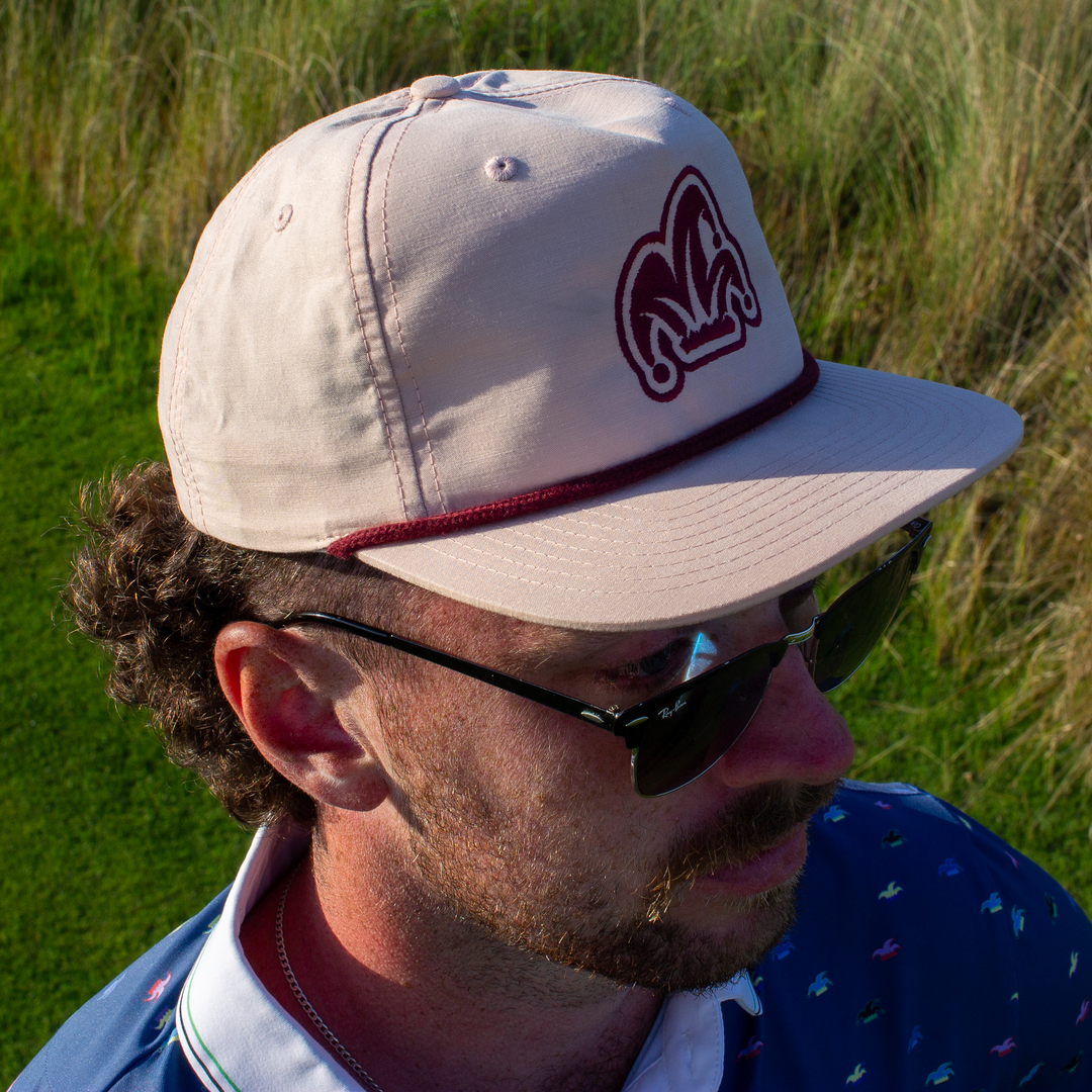 A golfer wearing a pink rope hat and a blue polo looks at the golf shot he is about to hit.