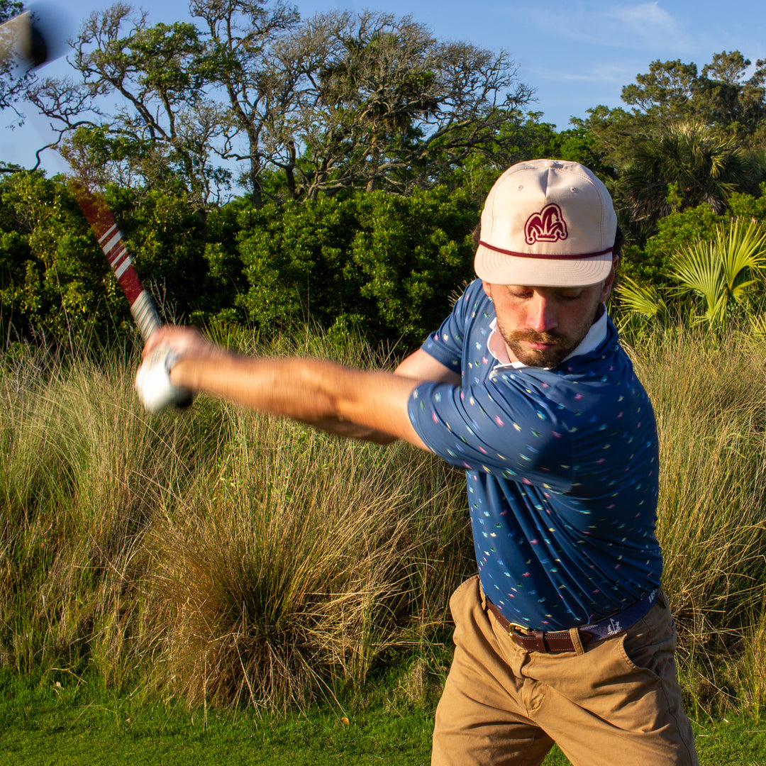 A golfer wearing a blue polyester-spandex polo hits his driver.