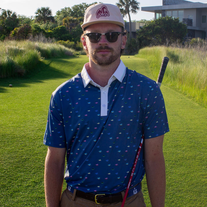 A Golfer wearing a blue polo with a white collar looks at the camera before hitting his golf shot.