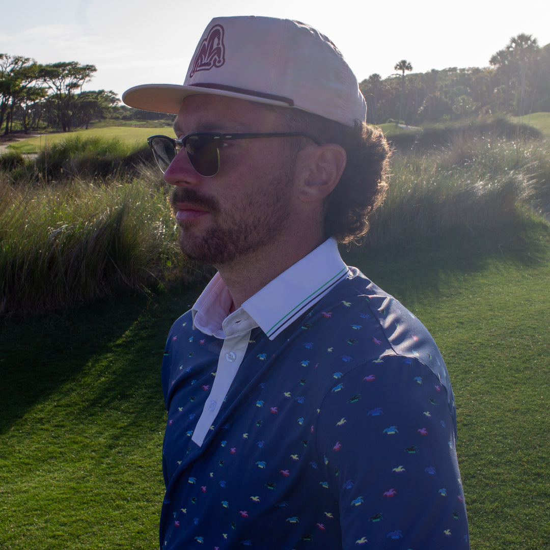 A golfer wearing a blue performance polo looks at the hole he is about to play.